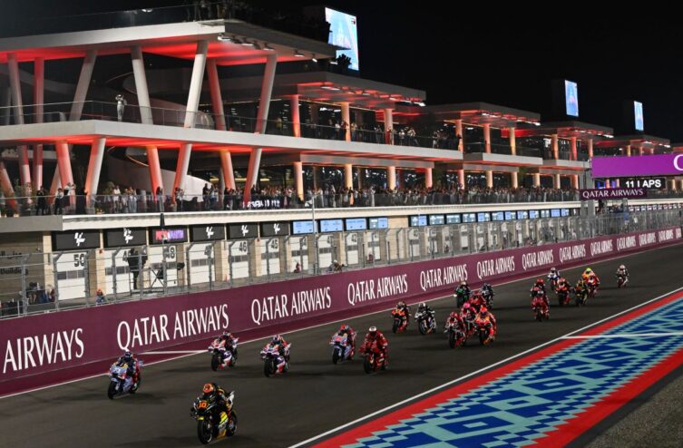 MotoGP riders lined up on the Losail start grid under floodlights preparing for a night race