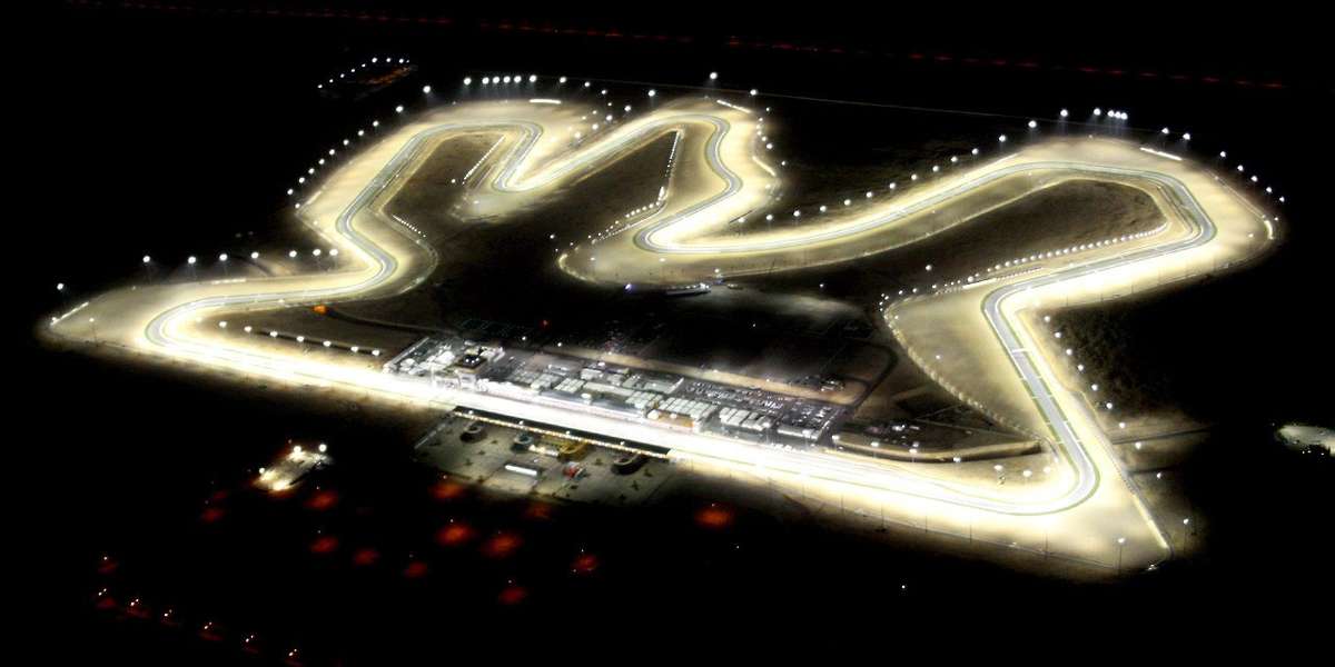 MotoGP bikes approaching Turn 1 at Losail with riders tucked in under heavy braking