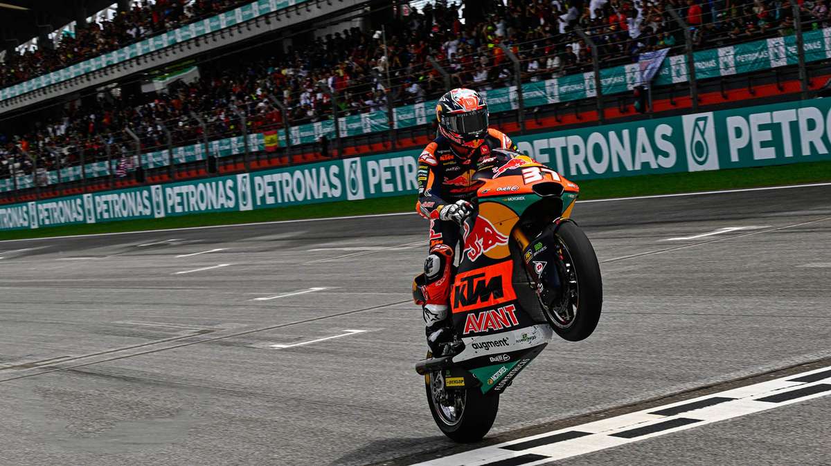 Pedro Acosta celebrating on the podium with the Moto3 rookie champion trophy, teammates and confetti in the background