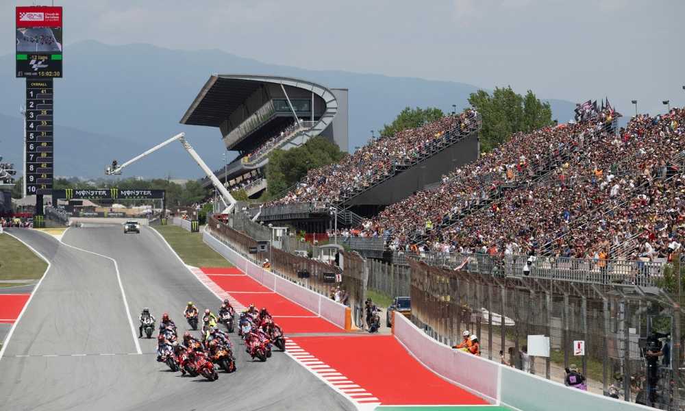 MotoGP riders approaching Turn 1 at Barcelona with historical runoff and safety barriers visible